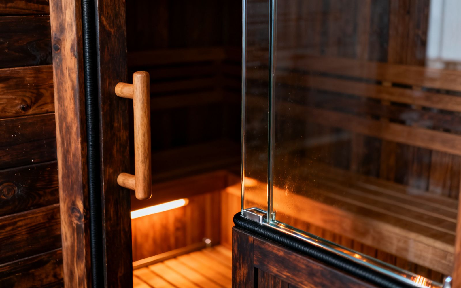 Detail einer Saunatür aus Glas und Holz, Beschlag und Dichtung im warmen Licht
